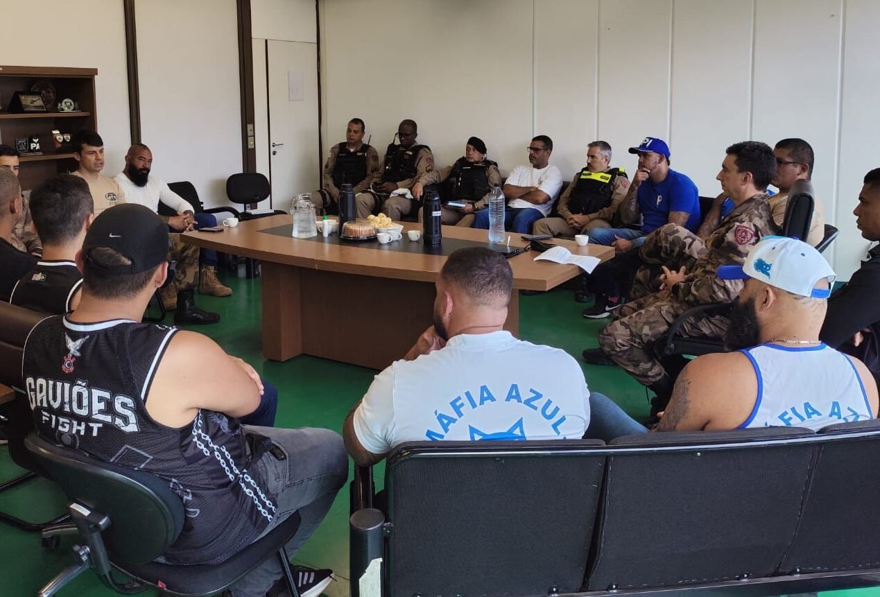 Membros da Polícia Militar de Minas Gerais e integrantes de torcidas organizadas de Cruzeiro e Corinthians sentados em cadeiras em torno de uma mesa de madeira (foto: PMMG/Divulgação)